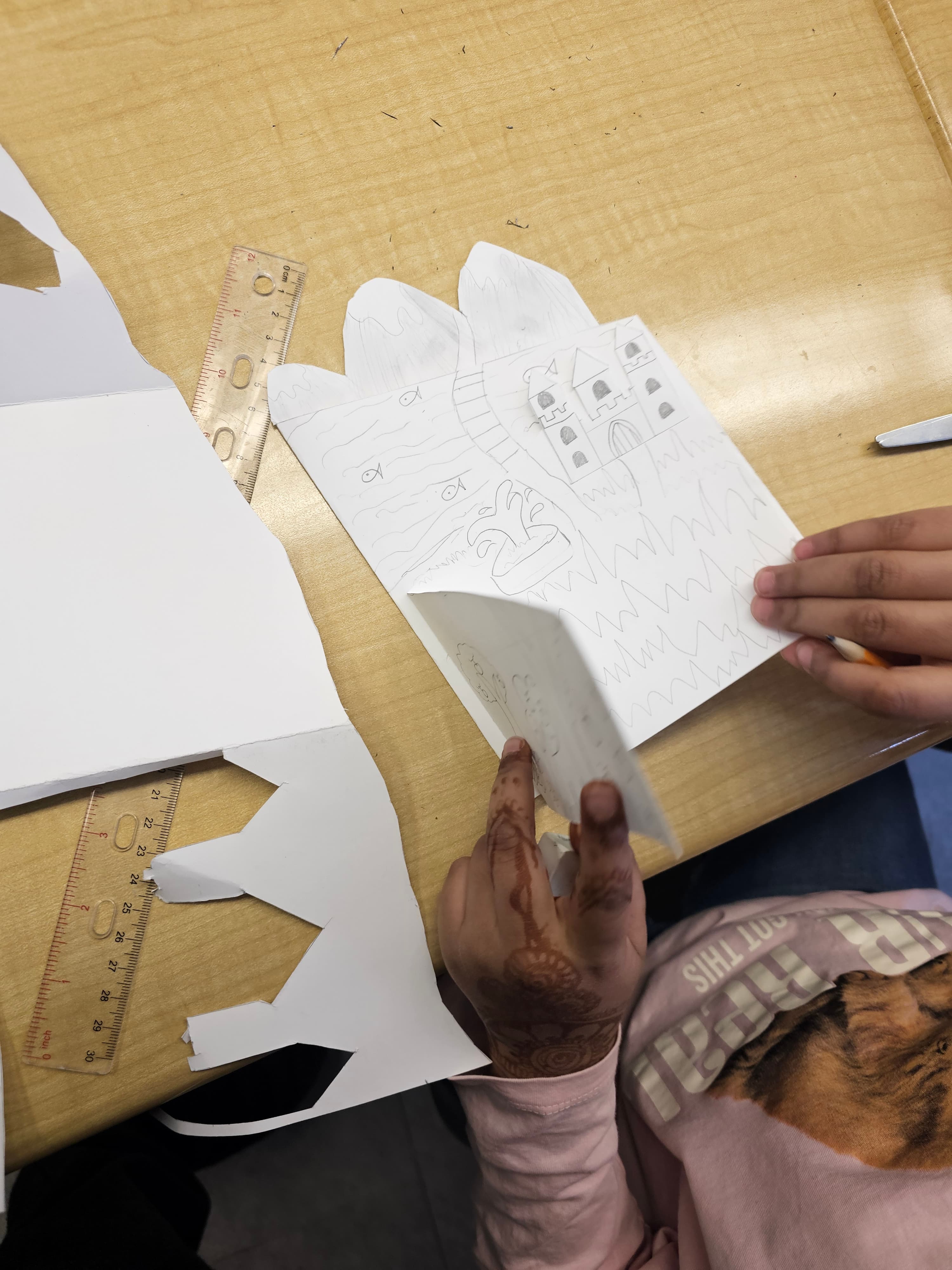 Close-up of hands assembling a layered paper landscape art project at Blue Willow Public School
