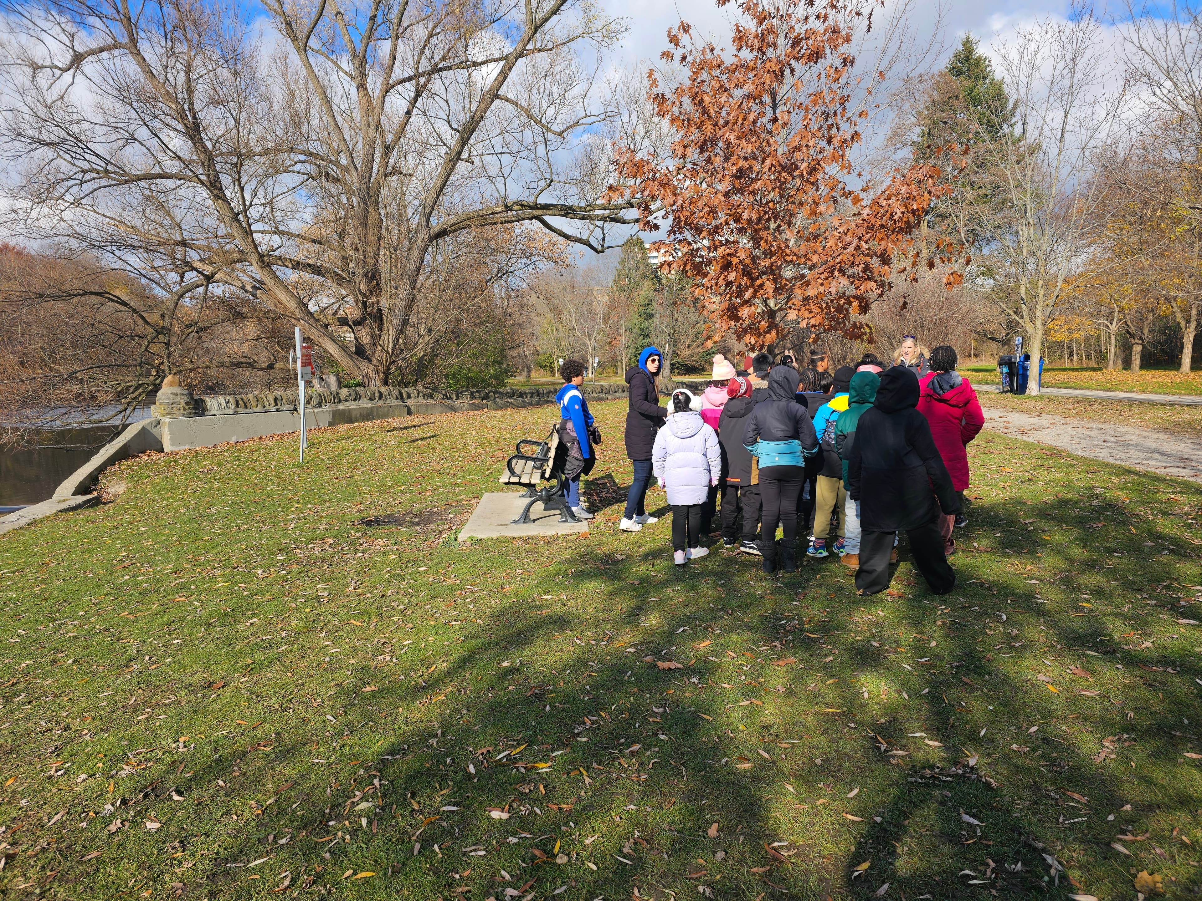 Class gathered beside a river during an outdoor field trip near Highview Public School, photographed from behind the group
